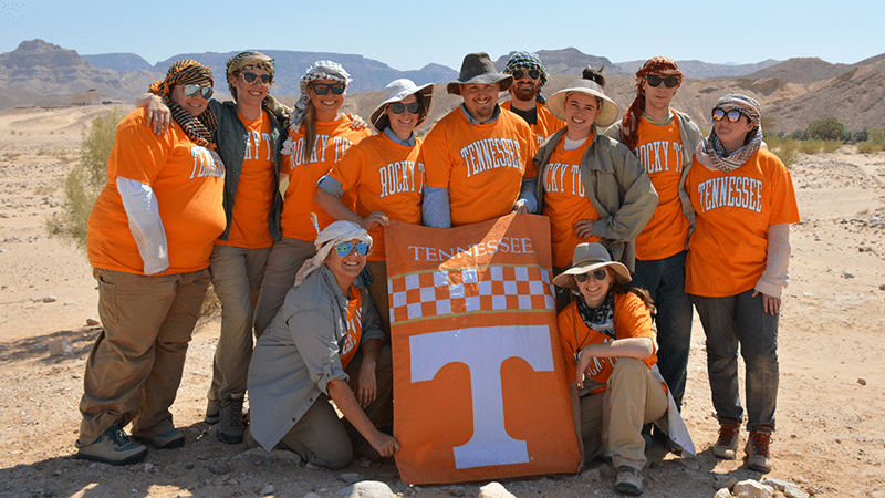 students in UT shirts, holding UT flags in a Jordanian desert during study abroad